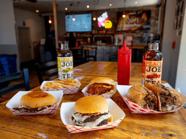 Halal smashburgers, ribeye cheesesteak, loaded fries and chicken sandwich on a wooden table at Cousin's Burger