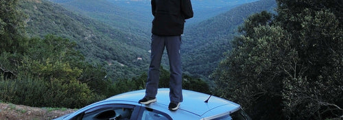 Haris Tagari standing on the roof of his silver Toyota Yaris above a green valley in Normandy, France