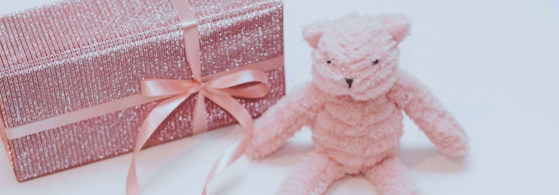 A soft pink teddy bear sitting beside a wrapped gift box with a ribbon