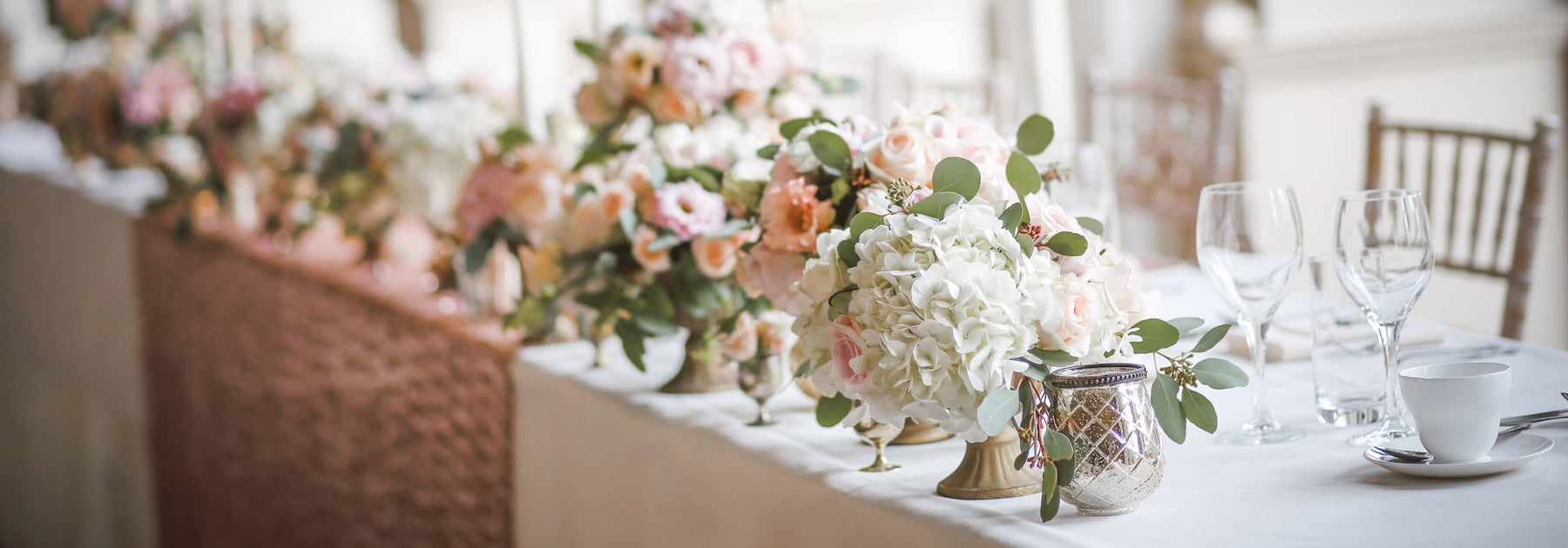 An elegant wedding reception table set with pale roses, hydrangeas and glassware