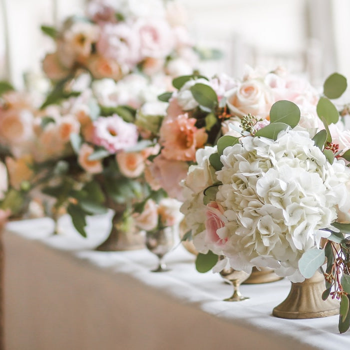 An elegant wedding reception table set with pale roses, hydrangeas and glassware