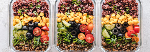 Three glass lunch containers packed with rice, lentils, corn and fresh vegetables