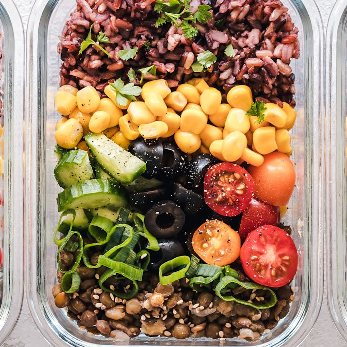 Three glass lunch containers packed with rice, lentils, corn and fresh vegetables