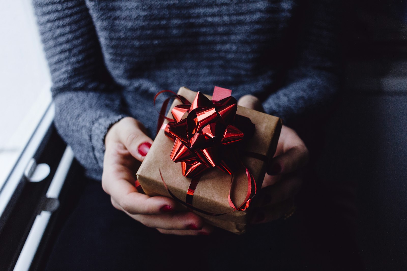 Hands holding a small gift wrapped in brown paper with a red bow