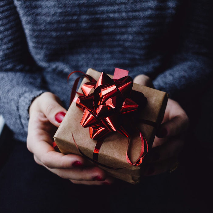 Hands holding a small gift wrapped in brown paper with a red bow