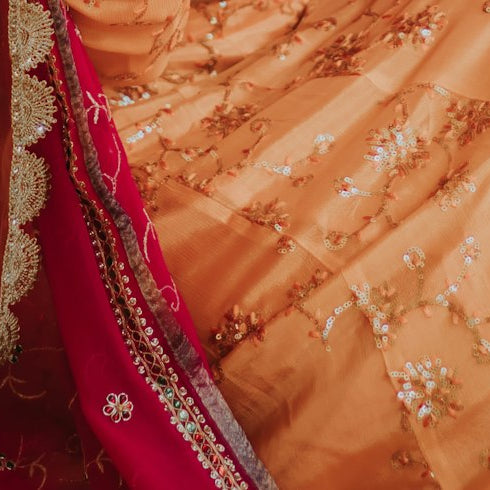 Close-up of a red and gold embroidered wedding outfit with an orange dupatta at a Muslim wedding