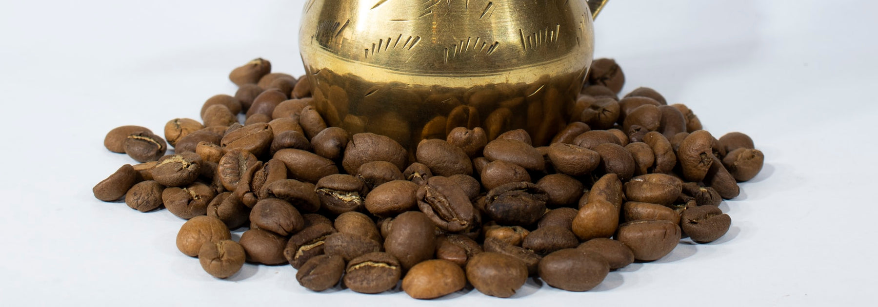 Traditional brass Arabic coffee dallah surrounded by roasted coffee beans