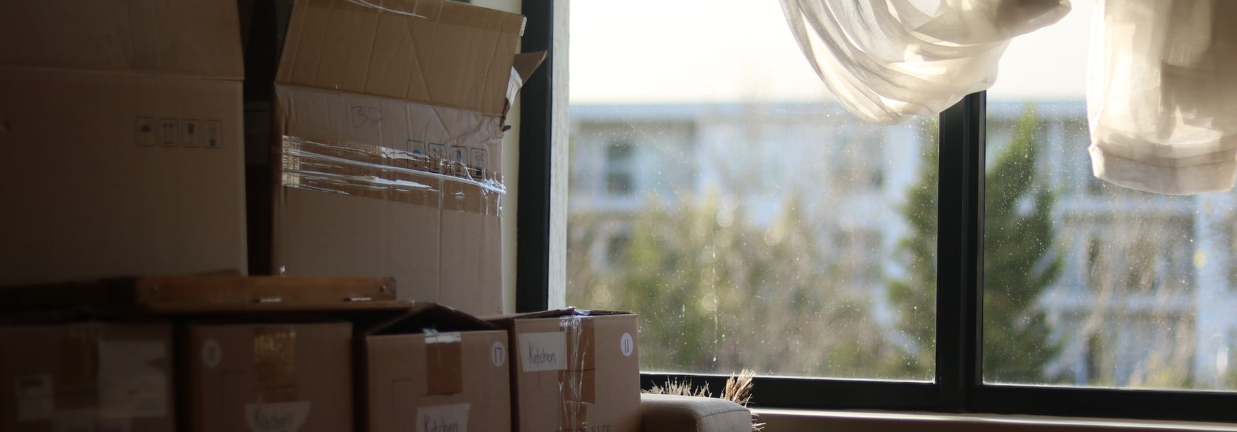 Labeled moving boxes stacked by a sunlit window in a new home