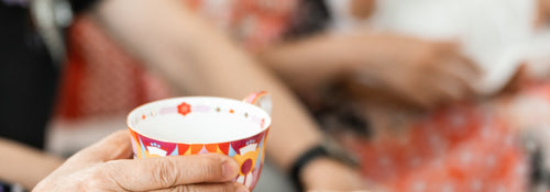 A hand passing a small patterned teacup to someone at a family gathering