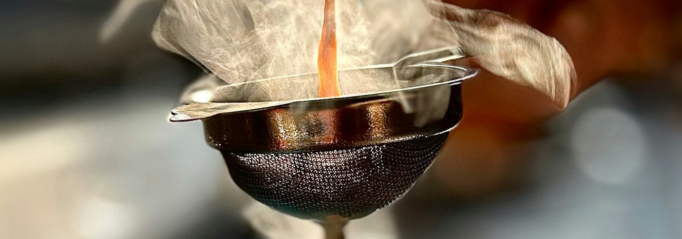 Hot chai being poured through a metal strainer with steam rising