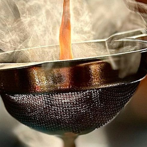 Hot chai being poured through a metal strainer with steam rising