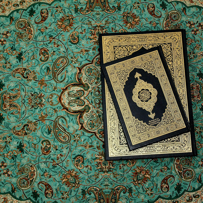 A Quran resting on an ornate turquoise prayer rug