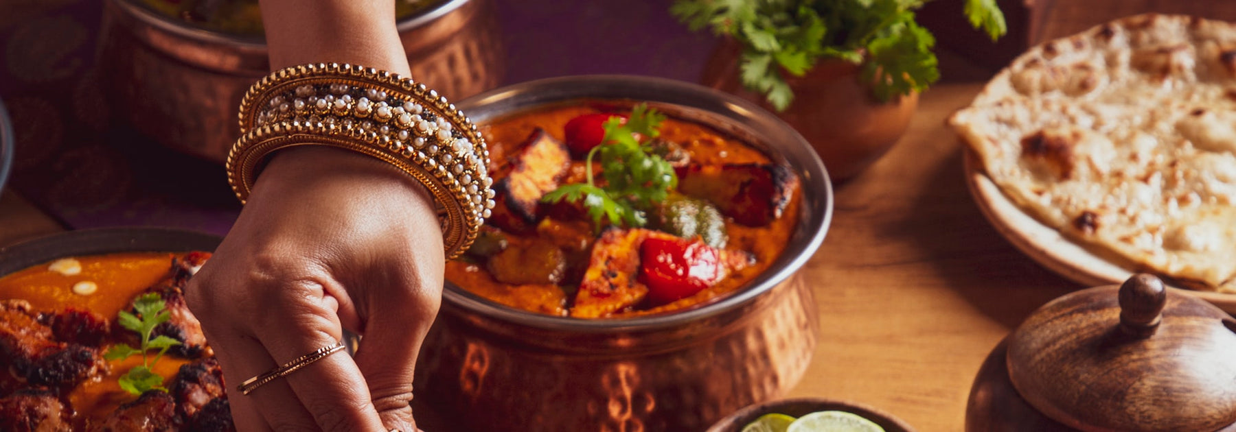 A South Asian dinner spread with curries, naan and kebabs in copper bowls