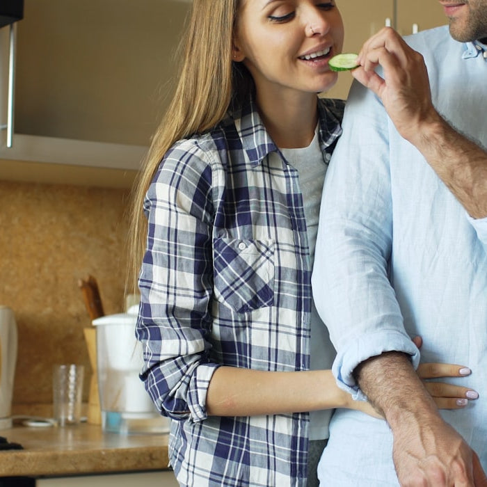 A husband and wife smiling together while cooking breakfast in a bright modern kitchen