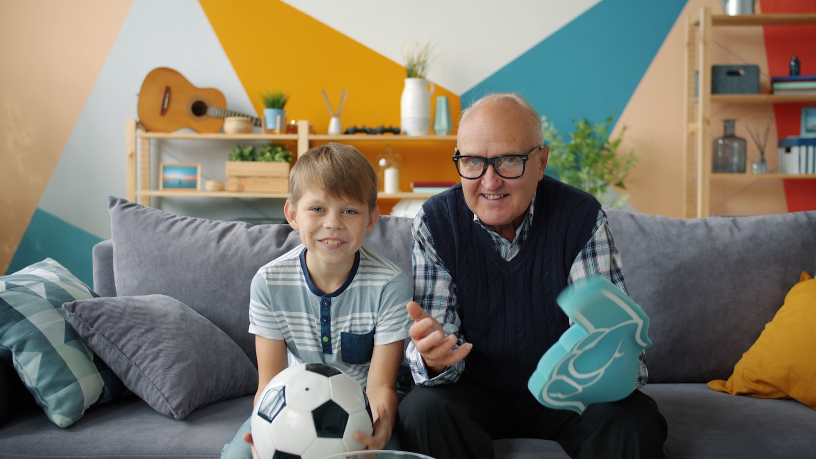 A grandfather and grandson cheering on the couch with a soccer ball during a match