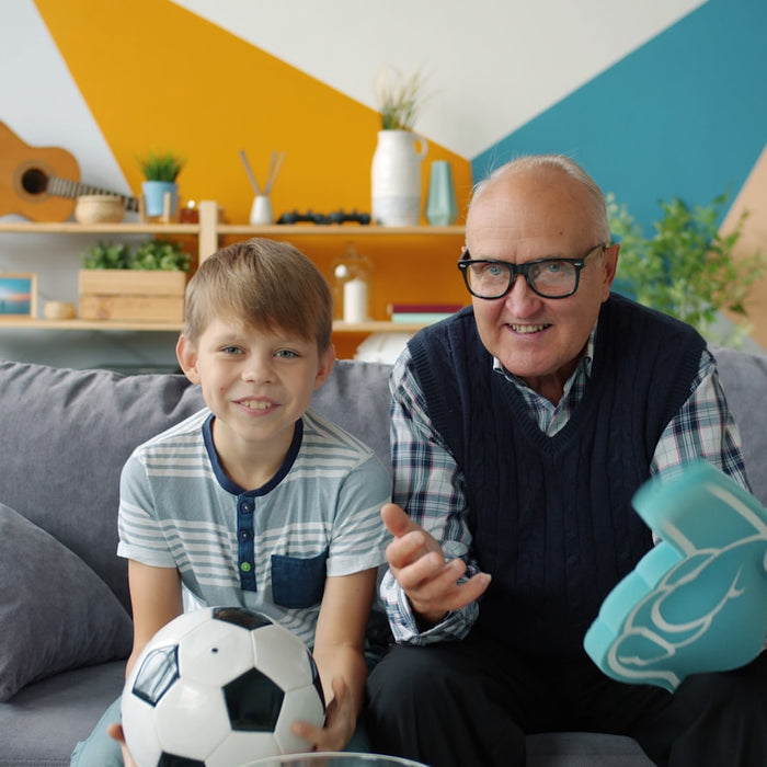 A grandfather and grandson cheering on the couch with a soccer ball during a match