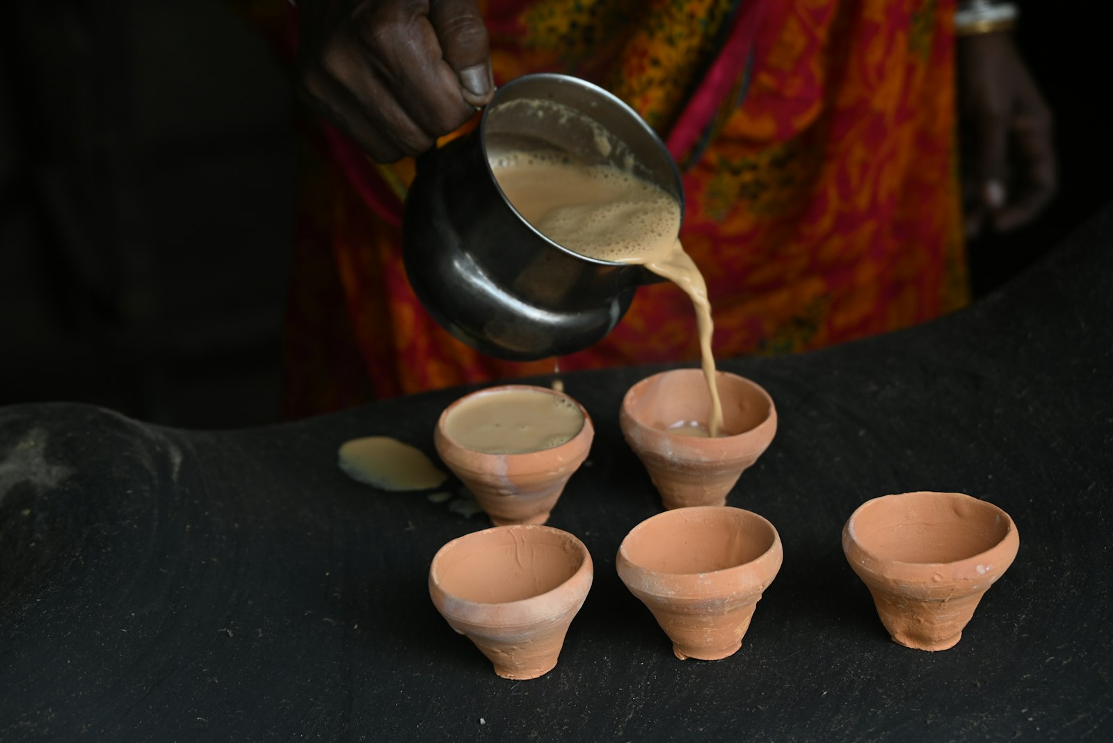 Chai being poured from a steel pot into small clay cups