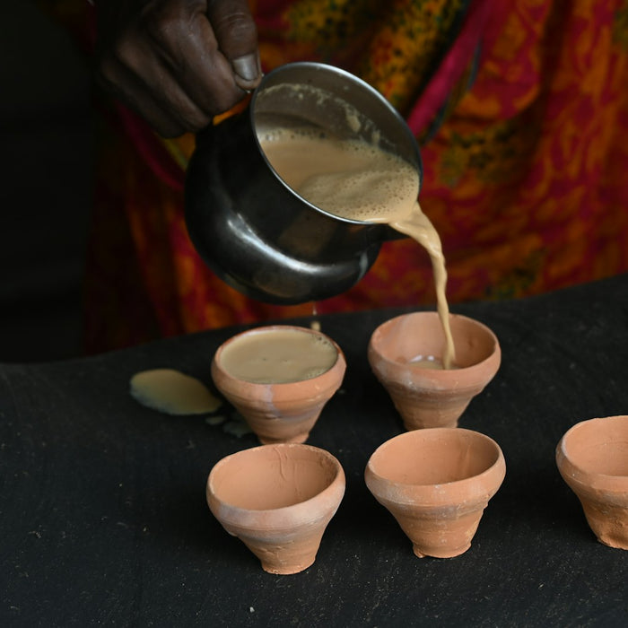 Chai being poured from a steel pot into small clay cups
