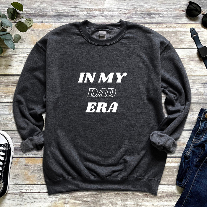 a sweater that says in my dad era next to a pair of jeans